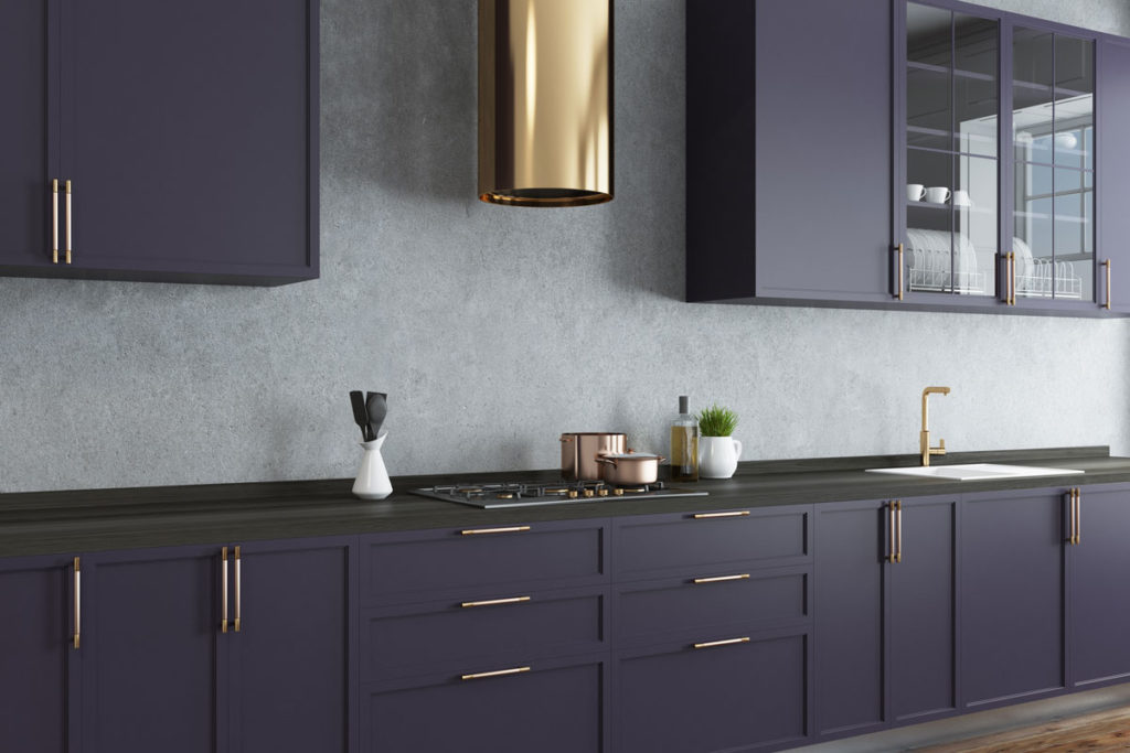 A kitchen with dark purple cabinets, a black counter top and brass accents