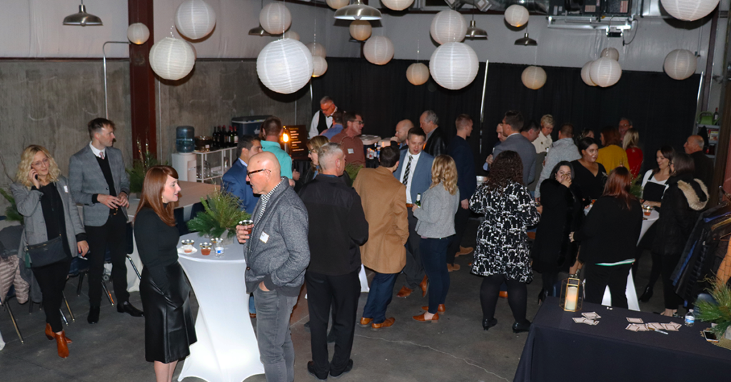 An industrial space decorated for a party with paper lanterns. There are many people in the talking and drinking cocktails. 