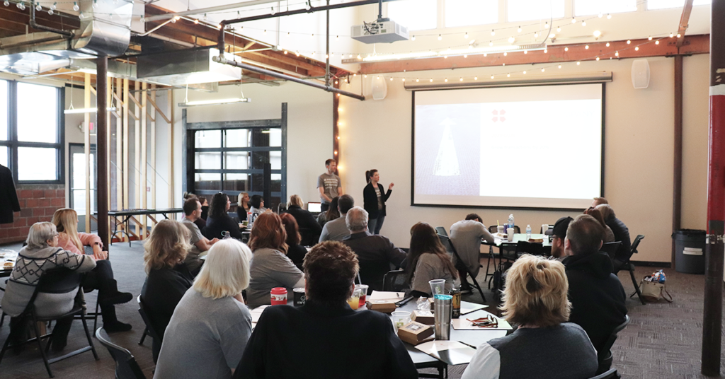 Ryan and Susan speaking in front of a room full of people. 